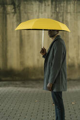 Junger Mann mit gelbem Regenschirm, der auf dem Fußweg steht und starrt - EGAF01508