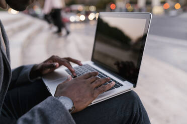 Mann, der im Freien sitzend am Laptop arbeitet - EGAF01515
