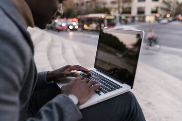 Junger Mann, der einen Laptop benutzt, während er im Freien sitzt - EGAF01516
