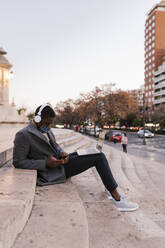 Man wearing face mask using mobile phone while sitting with laptop on steps - EGAF01521