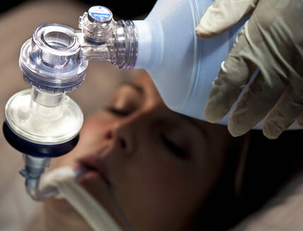 Hand eines Arztes, der einem Patienten auf der Intensivstation eine Sauerstofftasche reicht - UKOF00111