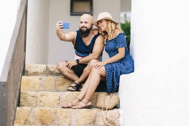 Freunde machen ein Selfie mit ihrem Smartphone, während sie auf den Stufen des Dorfes Binibeca sitzen, Menorca, Spanien - DGOF01810