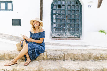 Fröhliche Touristin mit Hut auf dem Fußweg vor einem Haus im Dorf Binibeca, Menorca, Spanien - DGOF01816