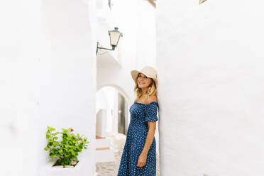 Schöne Frau mit Hut lehnt an einer weiß getünchten Mauer im Dorf Binibeca, Menorca, Spanien - DGOF01817