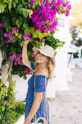 Lächelnde Touristin berührt Blumen auf einer Pflanze im Dorf Binibeca, Menorca, Spanien - DGOF01824