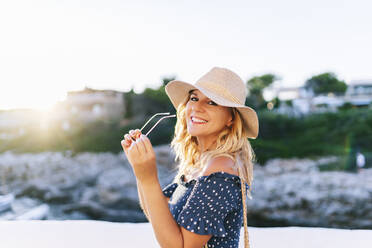 Lächelnde, schöne Frau mit Sonnenbrille vor einem klaren Himmel im Dorf Binibeca, Menorca, Spanien - DGOF01827