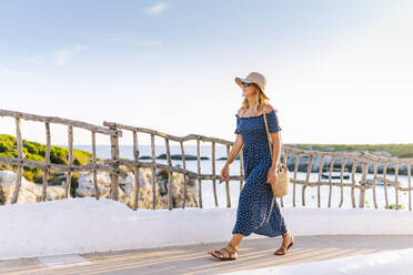 Weibliche Touristin mit Hut auf dem Fußweg gegen den Himmel im Dorf Binibeca, Menorca, Spanien - DGOF01830