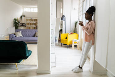 Woman drinking coffee while leaning on wall at home - GIOF10776