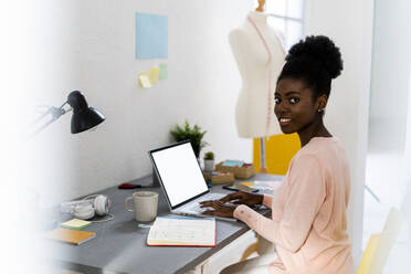 Lächelnde Modedesignerin, die im Büro zu Hause sitzt und einen Laptop benutzt - GIOF10794
