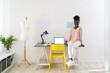 Young businesswoman smiling while sitting on table at home office - GIOF10808