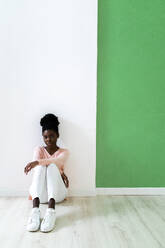 Junge Frau starrt, während sie gegen eine bunte Wand sitzt - GIOF10821