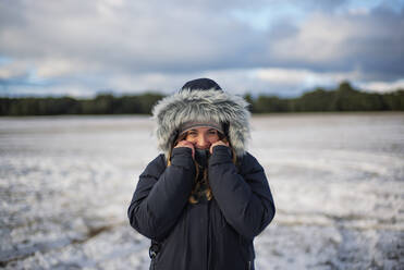 Frau in warmer Kleidung im Winter auf einem Feld stehend - OCMF02007