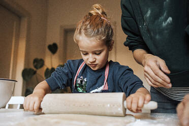 Girl helping her mother with rolling dough for cinnamon rolls in kitchen - DWF00557