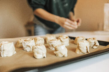 Arranged cinnamon rolls on baking sheet while woman in background at kitchen - DWF00563