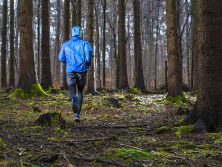 Junger Mann beim Joggen inmitten von Bäumen im Wald im Winter - STSF02766