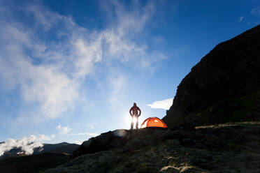 Woman standing by tent at sunrise, Iceland - MINF15777