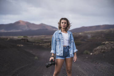 Junge Frau steht mit Kamera auf dem Fußweg am Vulkan El Cuervo, Lanzarote, Spanien - SNF00958