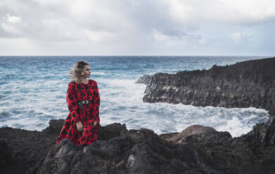 Junger Tourist schaut weg, während er in Los Hervideros, Lanzarote, Spanien, am Meer steht - SNF00975