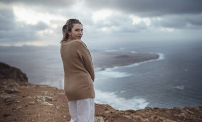 Woman staring while standing on mountain against Famara Beach, Lanzarote, Spain - SNF00989