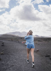 Young tourist smiling while walking on footpath at Volcano El Cuervo, Lanzarote, Spain - SNF00991