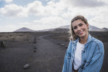 Junge Frau lächelt, während sie am Vulkan El Cuervo steht, Lanzarote, Spanien - SNF00993