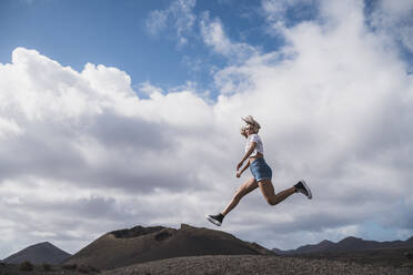 Junge Frau läuft gegen den Himmel am Vulkan El Cuervo, Lanzarote, Spanien - SNF00995