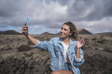 Lächelnder Tourist, der ein Selfie mit seinem Mobiltelefon macht, während er am Vulkan El Cuervo steht, Lanzarote, Spanien - SNF00997