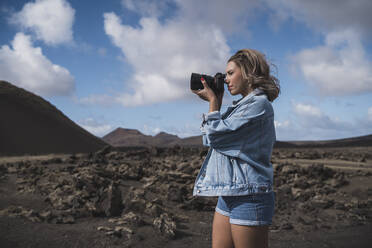 Forscher, der durch die Kamera fotografiert, während er gegen den Himmel am Vulkan El Cuervo steht, Lanzarote, Spanien - SNF01000