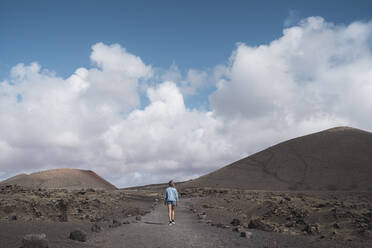 Explorer walking on footpath against sky at Volcano El Cuervo, Lanzarote, Spain - SNF01001