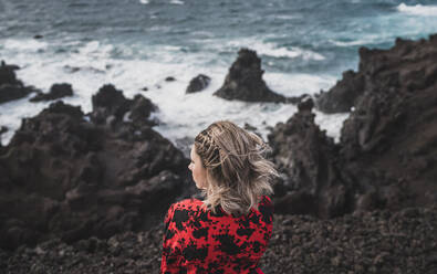 Junge Frau mit Blick auf das Meer, während sie in Los Hervideros, Lanzarote, Spanien steht - SNF01008