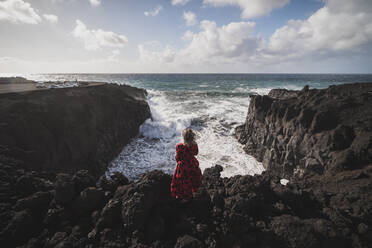 Frau mit Blick auf das Meer, während sie auf einem Berg in Los Hervideros, Lanzarote, Spanien steht - SNF01010