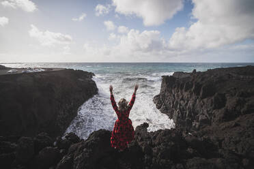 Unbekümmerte Frau mit erhobenen Armen am Meer bei Los Hervideros, Lanzarote, Spanien - SNF01011