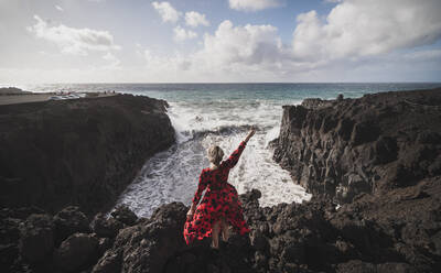 Young woman showing peace gesture while standing on mountain at Los Hervideros, Lanzarote, Spain - SNF01012