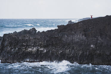 Frau steht mit ausgestreckten Armen auf einem Berg in Los Hervideros, Lanzarote, Spanien - SNF01013