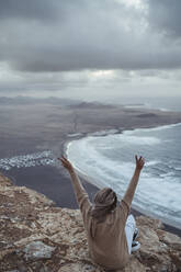 Sorgloser Tourist mit erhobener Hand auf einem Berg am Strand von Famara, Lanzarote, Spanien - SNF01023