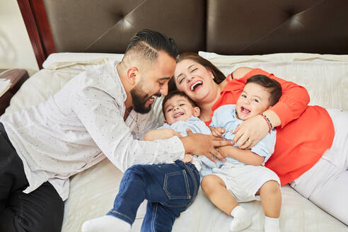 Von oben spielerische Hispanic Vater kitzeln liebenswert lachende Kinder und Mutter auf dem Bett liegen und Spaß haben zu Hause - ADSF20194