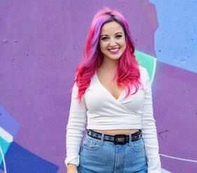 Modern millennial hipster female with dyed long hair looking at camera while standing against bright colorful wall - ADSF20236