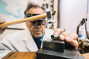 Fokussierter, erfahrener, reifer männlicher Meister mit Hammer und Meißel bei der Arbeit mit Edelsteinen in einer Schmuckwerkstatt - ADSF20262