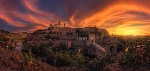 Blick über den Fluss der alten Stadt Toledo in Spanien mit mittelalterlichen Schlössern und Festungen bei Sonnenuntergang mit bewölktem Himmel und Reflexion im Flusswasser - ADSF20271