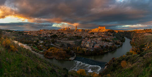 Blick über den Fluss der alten Stadt Toledo in Spanien mit mittelalterlichen Schlössern und Festungen bei Sonnenuntergang mit bewölktem Himmel und Reflexion im Flusswasser - ADSF20273