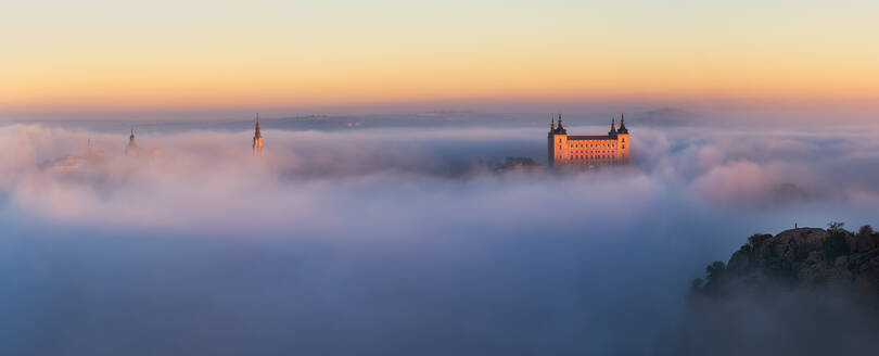 Drone Blick auf die Spitzen der alten Burgen zwischen dichten Wolken auf bunten Sonnenuntergang mit Hügeln am Horizont in Toledo - ADSF20275