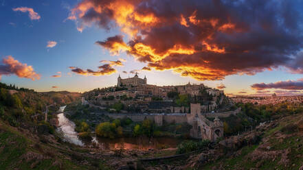 Panoramablick über den Fluss der alten Stadt Toledo in Spanien mit mittelalterlichen Schlössern und Festungen bei Sonnenuntergang mit bewölktem Himmel und Reflexion im Flusswasser - ADSF20276