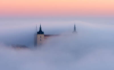 Drone Blick auf die Spitzen der alten Burgen zwischen dichten Wolken auf bunten Sonnenuntergang mit Hügeln am Horizont in Toledo - ADSF20280