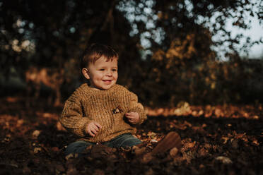 Cute smiling toddler sitting in forest during sunset - GMLF00938