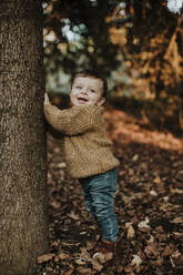 Cute toddler leaning on tree trunk in forest during sunset - GMLF00939