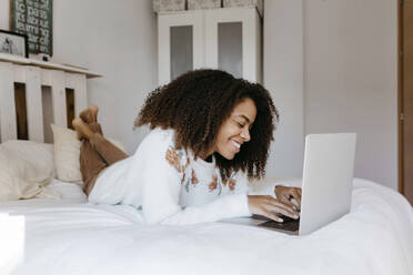 Young woman smiling while using laptop lying on bed at home - TCEF01466
