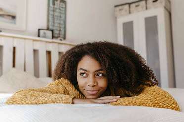 Thoughtful woman smiling while lying on bed at home - TCEF01477