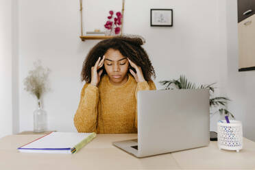 Tired woman with head in hands sitting by table at home office - TCEF01494