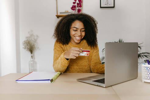 Junge Frau mit Kreditkarte, die einen Laptop benutzt, während sie zu Hause im Büro sitzt - TCEF01495