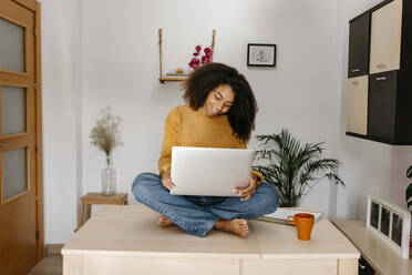 Young woman using laptop while sitting on table at home - TCEF01497